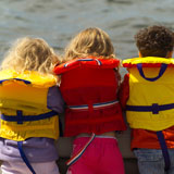 Rear+view+of+three+young+children+standing+side+by+side+wearing+life+jackets