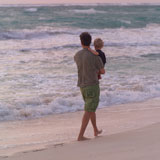 Parent+and+child+walking+along+beach+at+sunset