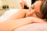 A+young+woman+relaxing+at+a+health+spa+while+having+a+hot+stone+massage