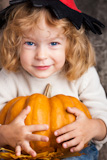 Happy smiling child in hat of witch holding a big orange pumpkin. Halloween concept