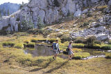 Hikers+Walking+Through+A+Wet+Meadow+Between+Rocky+Cliffs