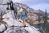 Female+Hiker+Walking+Along+A+Steep+Rocky+Cliff+Overlooking+A+Mountain+Lake