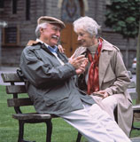 Elderly+Couple+Sitting+On+Park+Bench+And+Smiling