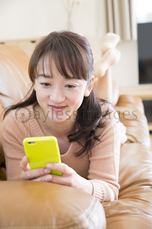 ソファで寝転んでスマホを見る女性 商用利用可能な写真素材 イラスト素材ならストックフォトの定額制ペイレスイメージズ