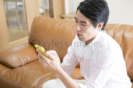 ソファに座ってスマホを見る男性 商用利用可能な写真素材 イラスト素材ならストックフォトの定額制ペイレスイメージズ