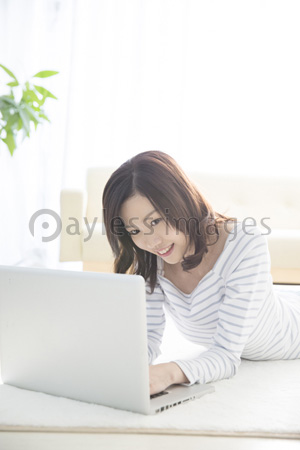 寝転んでノートパソコンを見る女性 ストックフォトの定額制ペイレスイメージズ