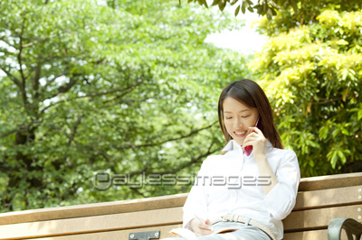 ベンチに座って電話するOL
