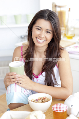 Beautiful woman having breakfast smiling at the camera sitting in the kitchen