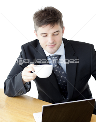 Charismatic businesman drinking coffee using his laptop at the breakfast table