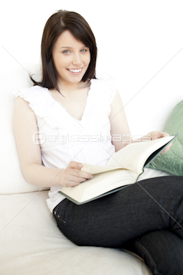 Cheerful woman reading a book sitting on a sofa