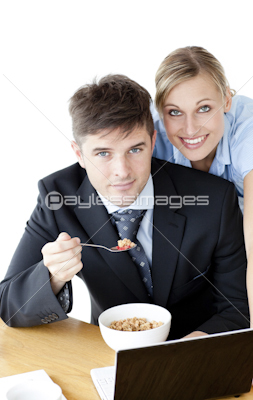 Enamored couple of businesspeople smiling at camera eating cereals