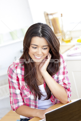 Glowing woman using her laptop sitting sitting in the kitchen