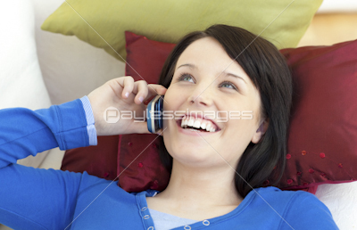 Happy teen girl talking on phone lying on a sofa