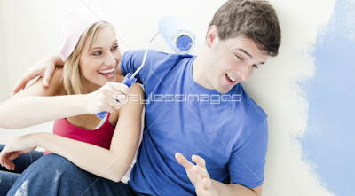 Laughing couple having fun while painting a room