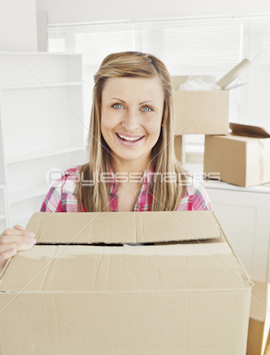 Positive woman holding a box standing in her new house looking at the camera