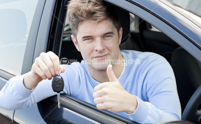 Positive young man holding a key sitting in a car