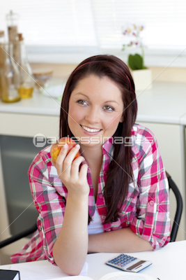 Radiant woman holding an apple sitting in the kitchen
