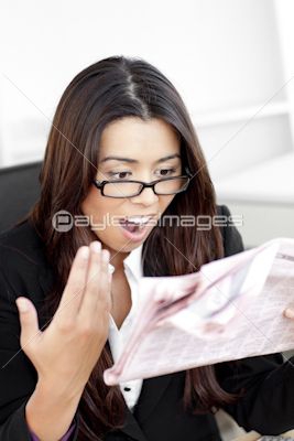 Shocked businesswoman looking at the newspaper in her office