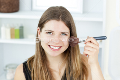 Smiling woman putting powder on her face smiling at the camera in the bathroom
