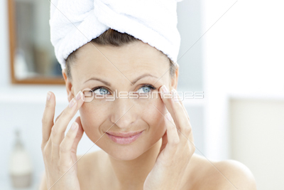 Smiling young woman putting moisturizer on her face