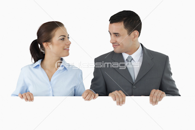 Business partners looking at each other while holding sign together
