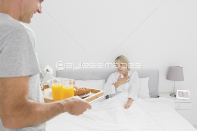 Cheerful couple having orange juice at breakfast in bed