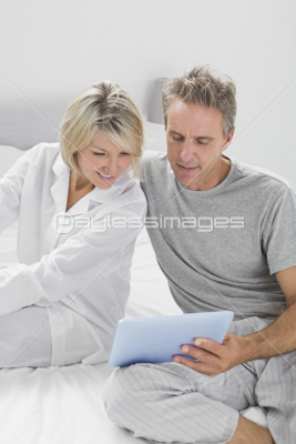 Couple using laptop sitting on bed