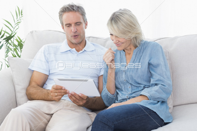 Happy couple using laptop together on the couch looking at camera
