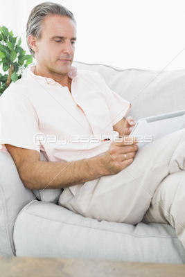 Happy man relaxing on his couch using tablet pc