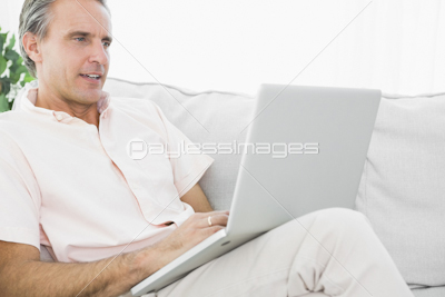 Happy man relaxing on his couch using tablet pc looking at camera