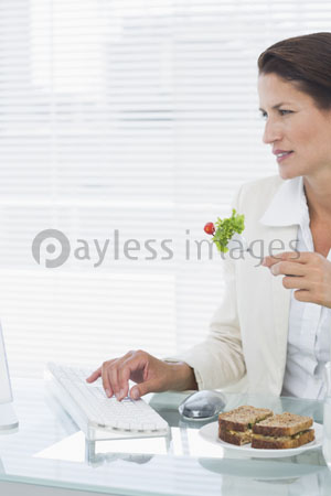 It is using computer about the female businessman [ it eats a salad at a desk ] of a between.