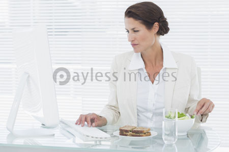 It is using computer about the female businessman [ it eats a salad at a desk ] of a between.