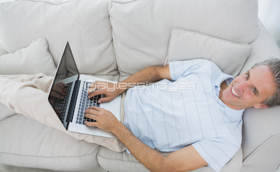 Man lying on couch typing on laptop