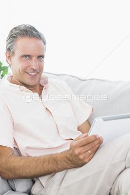Smiling man relaxing on his couch using tablet pc