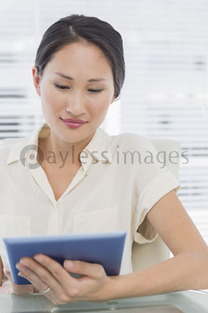 The female businessman is using the digital tablet at the desk.