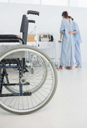 helping patient walks along a doctor with the wheelchair in a foreground.