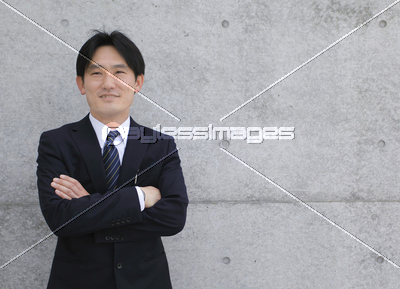 壁をバックに腕組みして立つビジネスマン ストックフォトの定額制ペイレスイメージズ