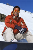 Snowboarder+sitting+on+hill+with+board+smiling+%28selective+focus%29