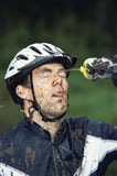 Man+outdoors+wearing+bicycle+helmet+and+splashing+water+on+face+%28selective+focus%29