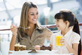 Mother+at+restaurant+with+daughter+eating+dessert+and+smiling+%28selective+focus%29
