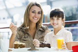 Mother+at+restaurant+with+daughter+girl+eating+dessert+and+smiling+%28selective+focus%29