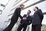 Three+businessmen+standing+outdoors+by+building+shaking+hands+and+smiling+%28high+key%2Fselective+focus%29