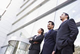 Three+businesspeople+standing+outdoors+by+building+smiling+%28high+key%2Fselective+focus%29