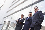 Three+businesspeople+standing+outdoors+by+building+smiling+%28high+key%2Fselective+focus%29