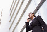 Businesswoman+standing+outdoors+by+building+on+cellular+phone+%28high+key%2Fselective+focus%29