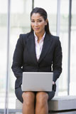 Businesswoman+sitting+outdoors+by+building+with+laptop+smiling+%28high+key%2Fselective+focus%29