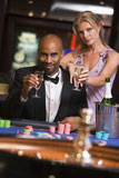 Couple+in+casino+at+roulette+table+holding+champagne+and+smiling+%28selective+focus%29