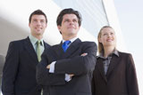Three+businesspeople+standing+outdoors+by+building+smiling