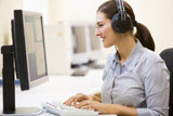 Woman+wearing+headphones+in+computer+room+typing+and+smiling