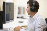Man+wearing+headphones+in+computer+room+typing+and+smiling